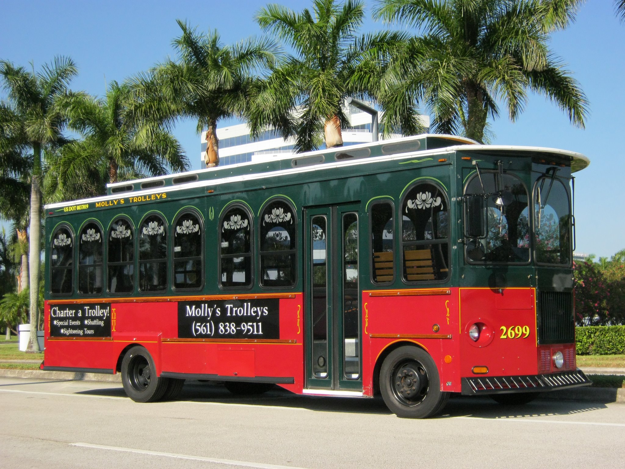 Vintage trolley parked in front of a palm tree in West Palm Beach, showcasing classic transportation against a tropical backdrop.